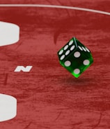 Two green dice with rounded edges are positioned on a red surface that seems to be part of a game board. The surface has white text and numbers on it, including the word 'LUCKYTOPSPIN' in capital letters.